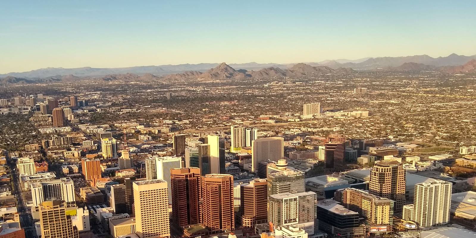 A city skyline seen from the air in late afternoon light, with mountains along the horizon.